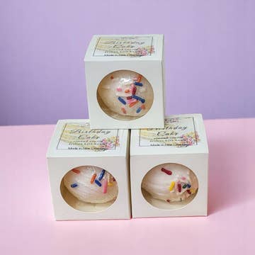 Three boxes of birthday cake-themed bath bombs on a pink