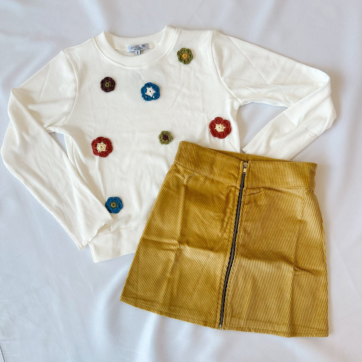 White long-sleeve shirt with colorful flower buttons and mustard yellow skirt