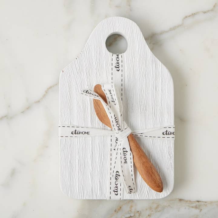Wooden cutting board with a wooden knife tied with a white ribbon on a marble surface